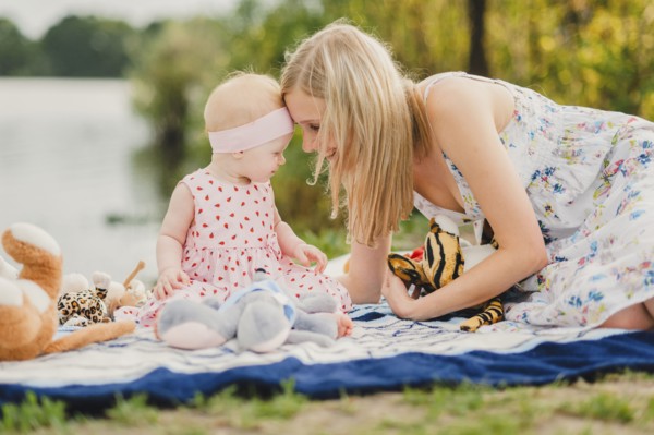 Mother and daughter playing with stuffed animals on blanket near lake