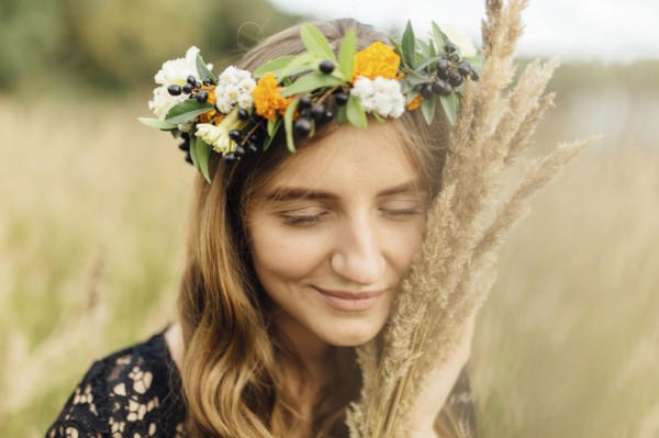 Middle Eastern woman wearing flower crown holding wheat to face