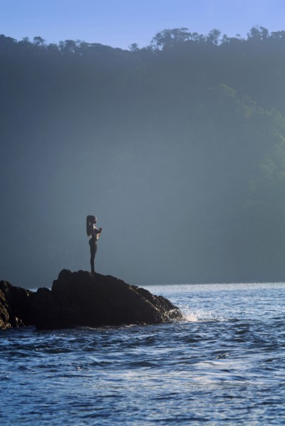 Mixed race woman standing on rock over ocean