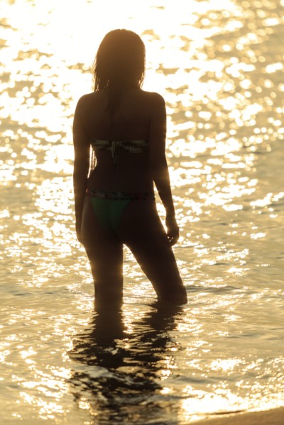 Silhouette of Mixed Race woman wading in ocean at sunset