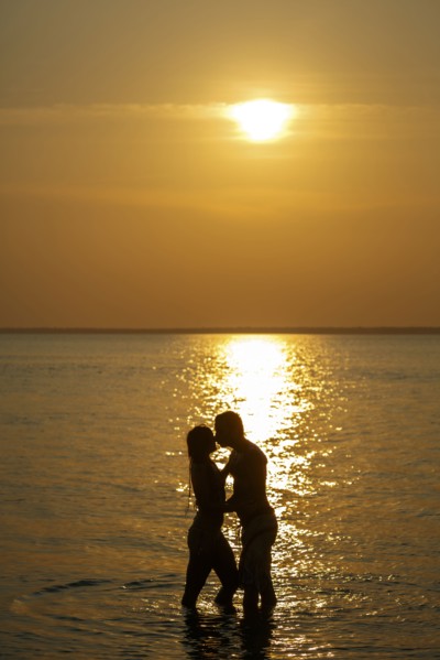 Silhouette of Caucasian couple kissing in ocean at sunset