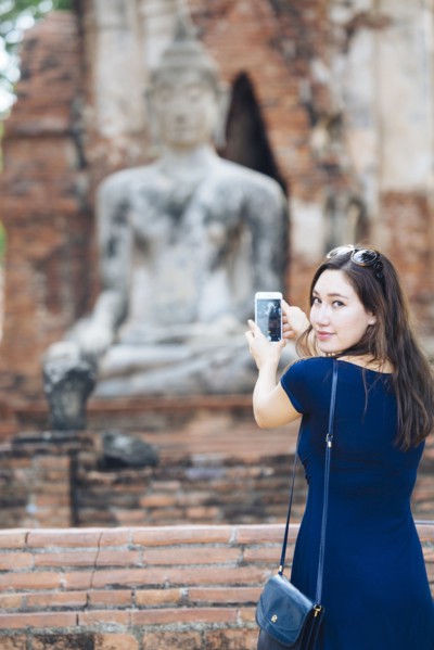 Asian woman photographing Buddha statue with cell phone