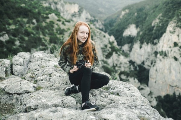 Portrait of smiling Caucasian woman sitting on rock holding camera