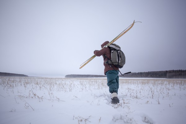 Mixed race man carrying skis in snowy field