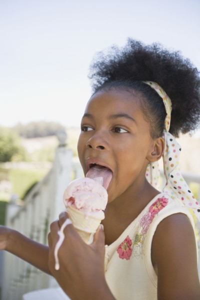Mixed race girl licking melting ice cream cone
