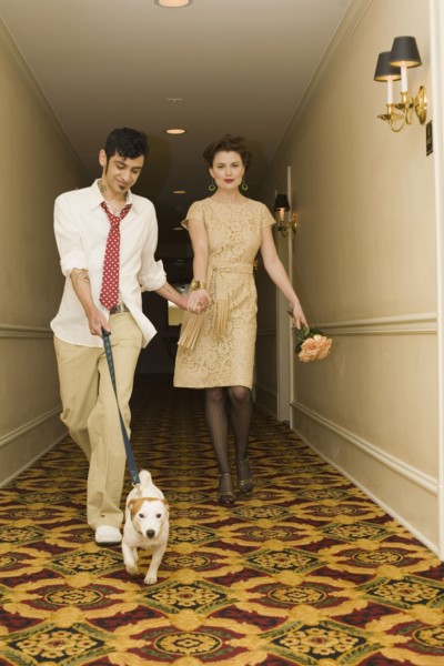 Young coupled dressed up walking down hotel hallway with dog