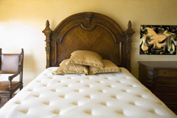 Large unmade bed with three pillows and wooden headboard