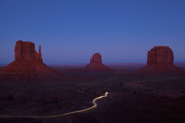 Long exposure of car driving past butte rock formations in desert landscape