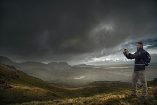 Caucasian hiker photographing storm clouds over landscape