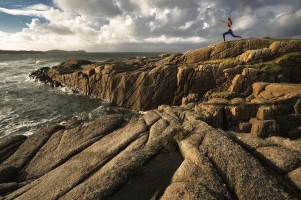 Distant Caucasian woman doing yoga on rocks near ocean