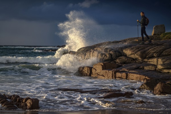 Distant Caucasian woman hiking on rocks near ocean