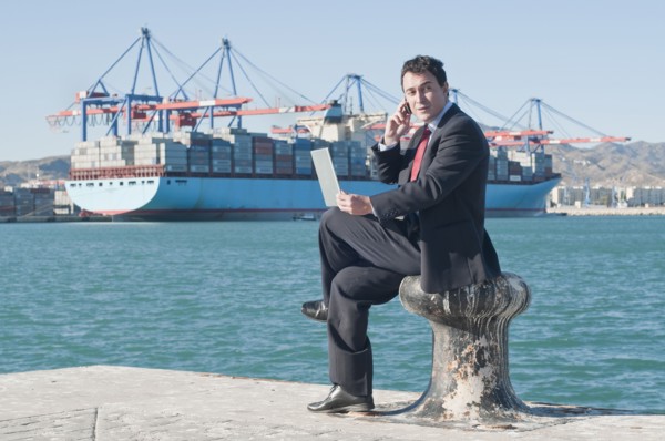 Hispanic businessman holding laptop with container ship in background
