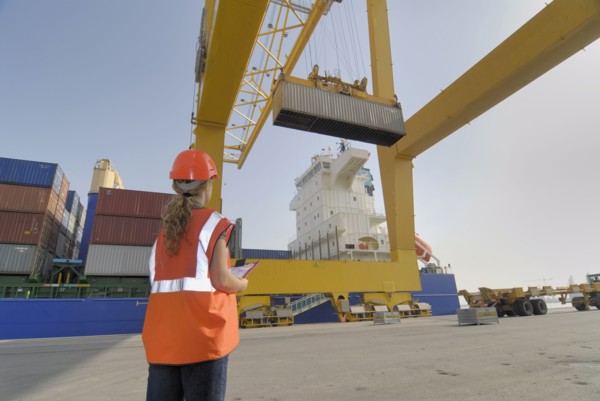Woman at docks watching container on straddle carrier