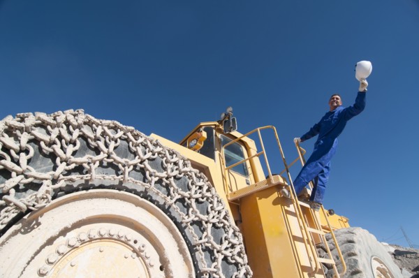 worker waving hard hat standing on mining machine