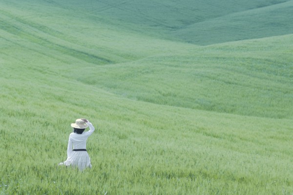 Woman in white dress walking through rolling hills of young wheat