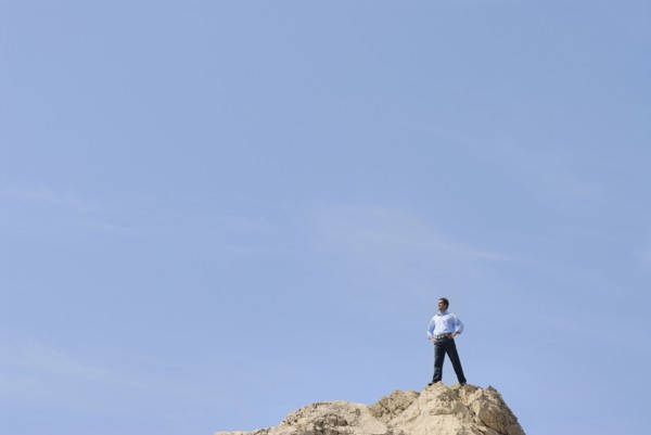Businessman standing on top of rock looking into distance