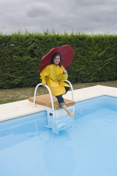 woman in rainwear tipping toe into swimming pool