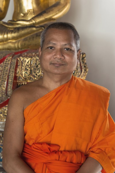 Thai Buddhist monk smiling near statue