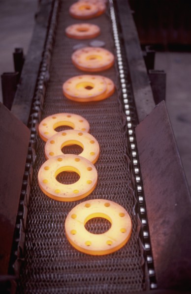 Glowing metal manufactured pieces on conveyor belt