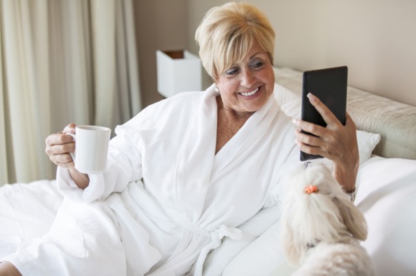 Older Caucasian woman and dog using digital tablet on bed