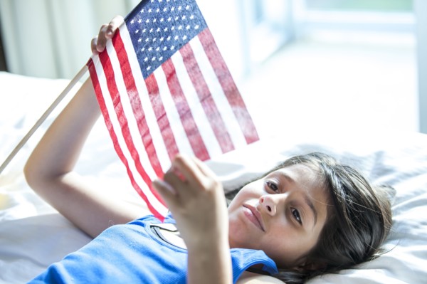 Hispanic girl holding American flag on bed