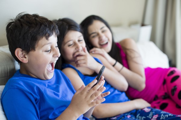 Hispanic siblings using cell phone on sofa