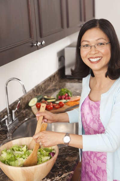 Chinese woman tossing salad in kitchen