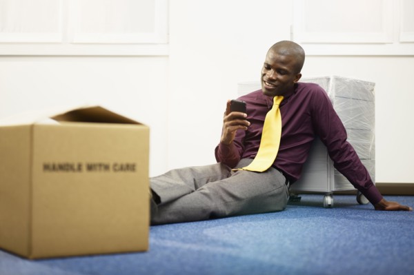 Black businessman sitting on floor text messaging
