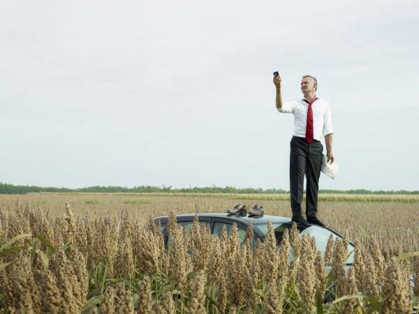 Caucasian businessman on top of car in field looking at gps device