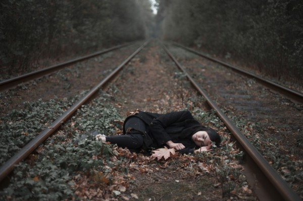 Caucasian woman laying between railroad tracks