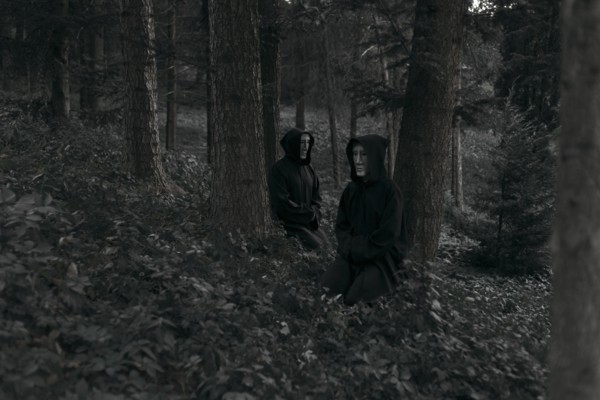 People wearing black robes and white masks sitting in forest