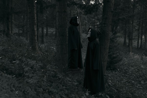 People wearing black robes and white masks standing in forest