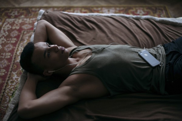 Black man laying on bed listening to music on cell phone