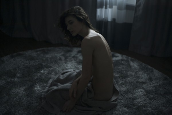 Portrait of nude Caucasian woman sitting on rug with blanket