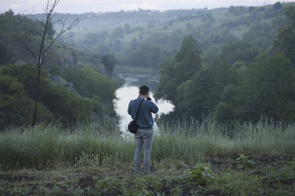 Caucasian man standing on hill photographing river