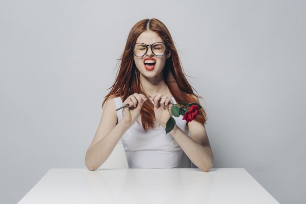 Caucasian woman sitting at windy table snapping stem of rose