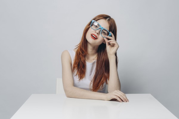 Pensive Caucasian woman sitting at table wearing blue eyeglasses