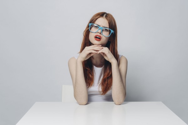 Angry Caucasian woman sitting at table wearing blue eyeglasses