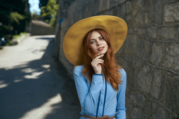 Smiling Caucasian woman wearing hat near stone wall