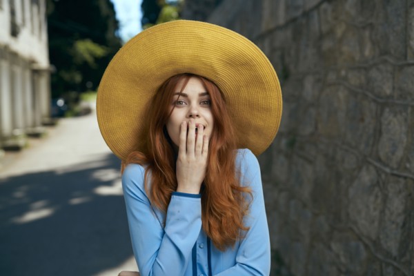 Surprised Caucasian woman wearing hat near stone wall