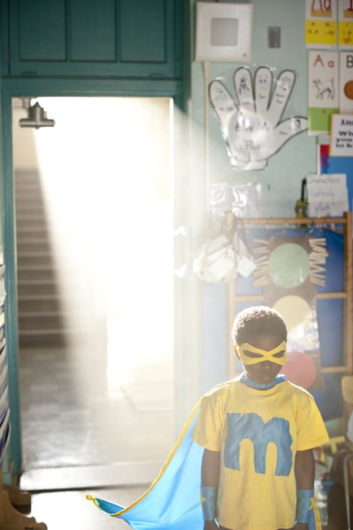 African American boy wearing superhero costume in classroom