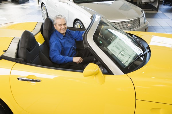 Hispanic car salesman sitting in new car