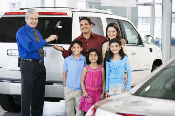 Hispanic car salesman handing car keys to family