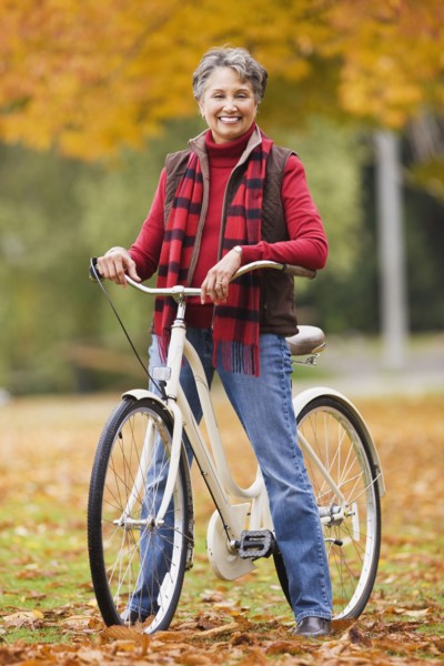 African woman standing with bicycle in park in autumn