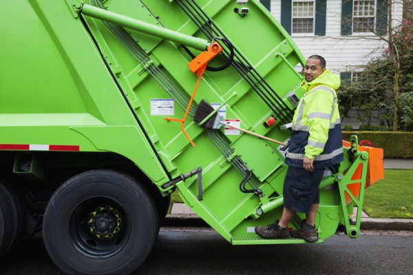 Pacific Islander man riding on garbage truck