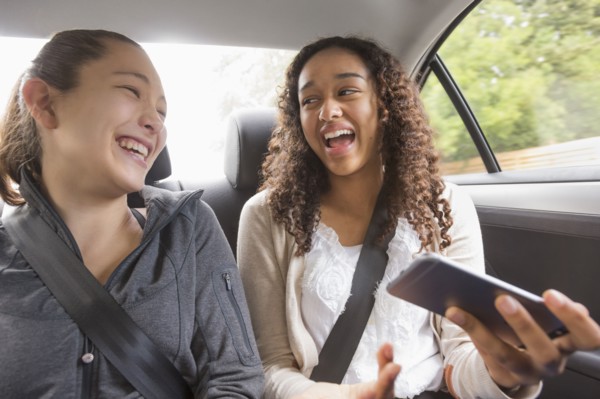 Teenage girls using cell phone in car back seat