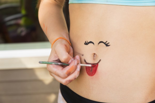 Mixed race girl painting face on stomach