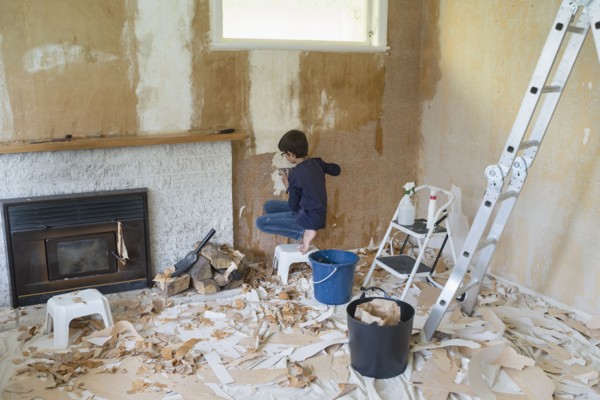 Mixed race boy stripping wallpaper in living room