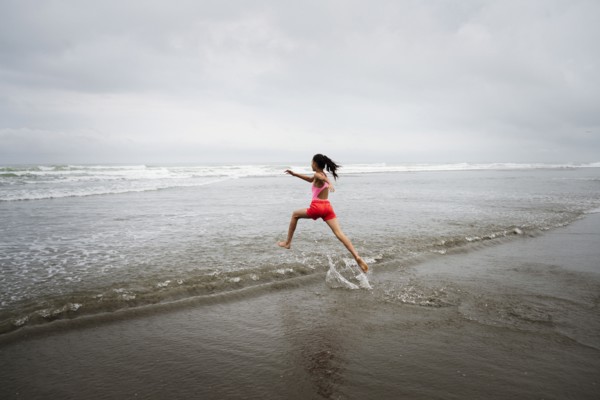 Mixed race girl running into ocean on beach