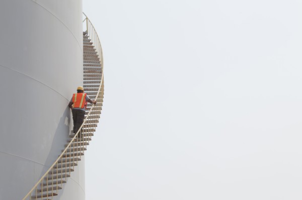 Mixed race worker climbing staircase on storage tank